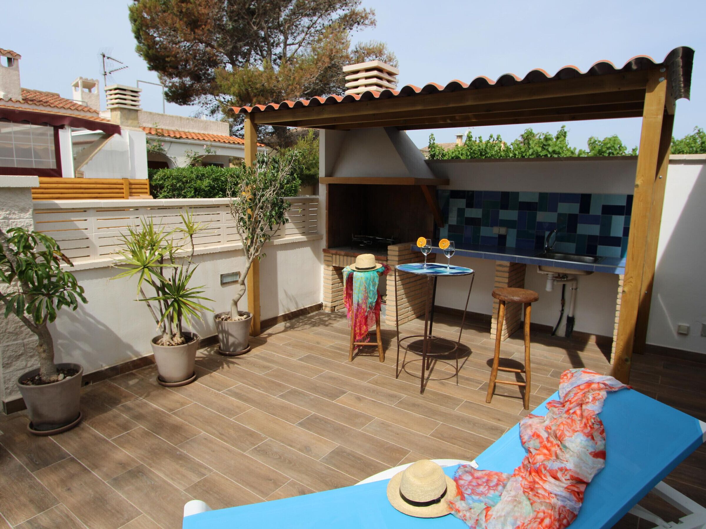 A patio with a blue lounge chair, a small table with two wine glasses, and a grill area.