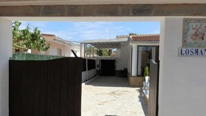 A covered outdoor area with a tiled floor, a wooden gate, and a building with a tiled roof. - Perfect Vacation Home: Private Pool, Near the Sea, Free WiFi, Pet-Friendly, Dog Beach. (Deltebre)