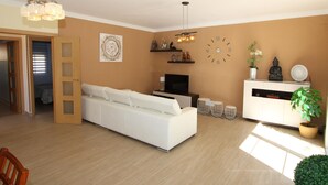 Ein modernes Wohnzimmer mit einem weißen Sofa, einem Fernseher, einer Uhr und dekorativen Gegenständen auf Regalen.