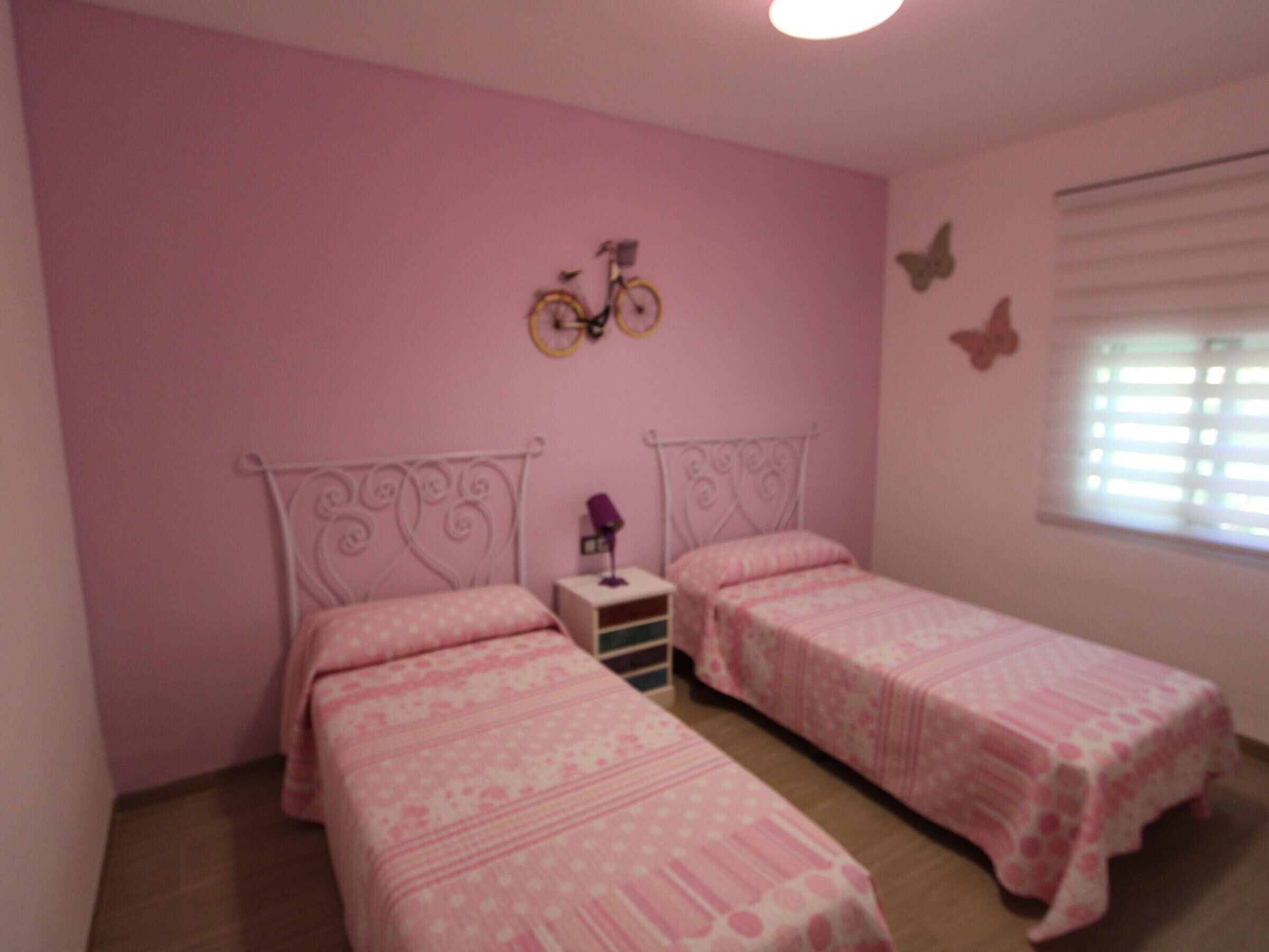 A bedroom with two beds, pink walls, and a window with blinds.
