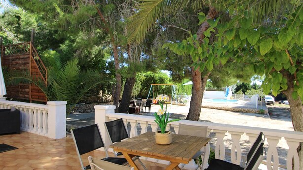 Eine Terrasse im Freien mit einem Holztisch und Stühlen, umgeben von einem weißen Zaun.