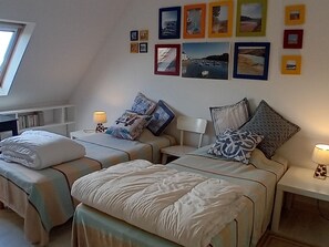 A bedroom with two beds, each with a bedside table and lamp, and a wall decorated with framed pictures.