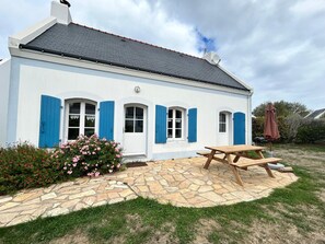 Un bâtiment blanc avec des volets bleus, une terrasse en pierre et une table de pique-nique.