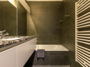 Een moderne badkamer met een grote spiegel, een wastafel met twee kommen, een bad en een handdoekrek.