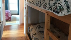 Un llit superposat amb roba de llit de motius florals, un sòl de fusta i una finestra amb cortines.