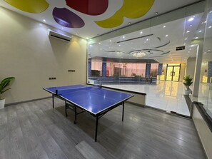 A ping pong table in a modern room with a glass wall, wooden flooring, and a ceiling with colorful geometric shapes.