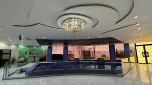 Un vestíbulo con una escalera central, una araña y una recepción.