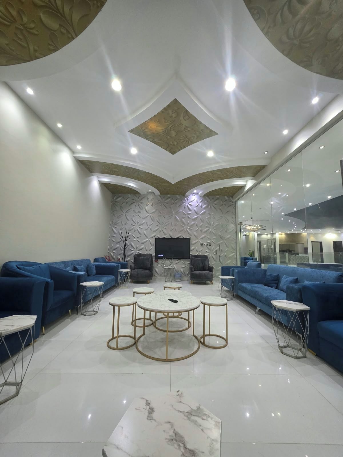 A modern living room with blue sofas, a central coffee table, and a flat-screen TV mounted on the wall.