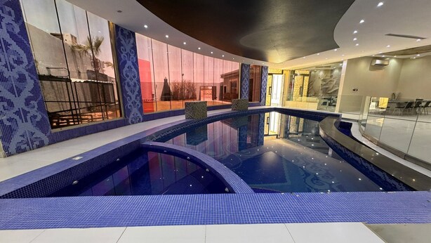 Una piscina interior moderna de diseño curvo, rodeada de paredes con motivos y un cerramiento de vidrio.