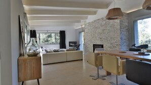 A modern living room with a stone wall, a wooden dining table, and a sofa. - Maison Contemporaine Avec Piscine à Mi-chemin Entre la Plage de Sa Tuna et Begur (Begur)