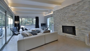A modern living room with a stone wall, a flat-screen TV, a sofa, and a glass door leading to an outdoor area. - Maison Contemporaine Avec Piscine à Mi-chemin Entre la Plage de Sa Tuna et Begur (Begur)