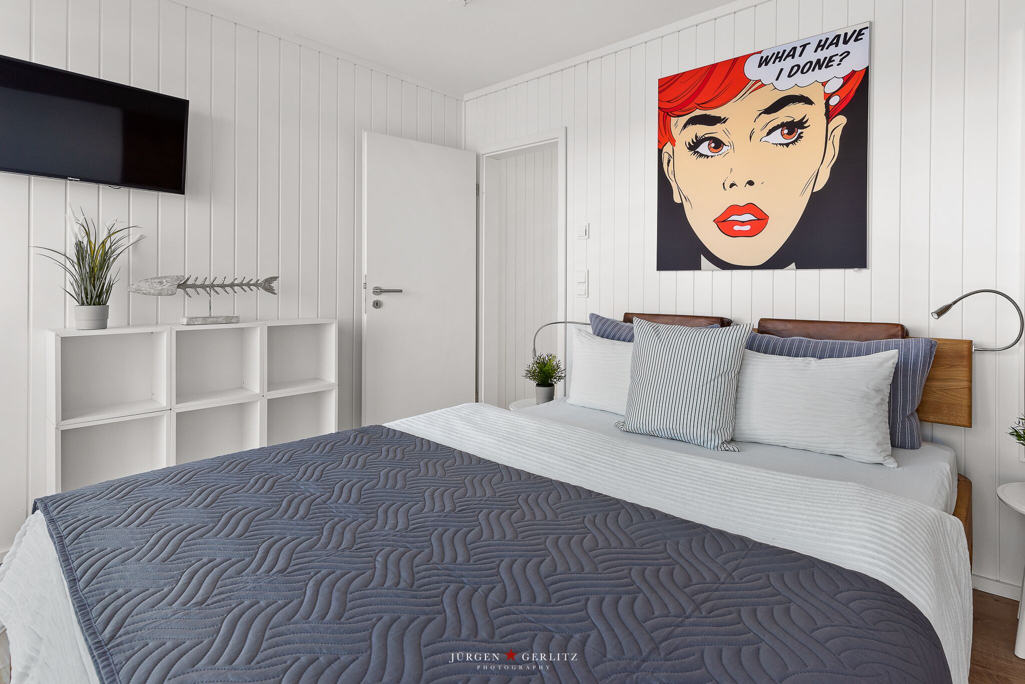 Une chambre à coucher moderne avec un lit, une télévision, une affiche et une plante.