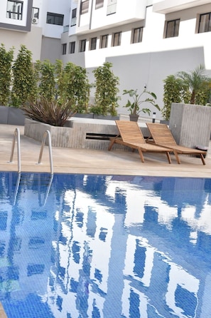 A swimming pool with lounge chairs and potted plants. - Cozy 2 Bedroom apt with Pool View & Gym Access! (kenitra)