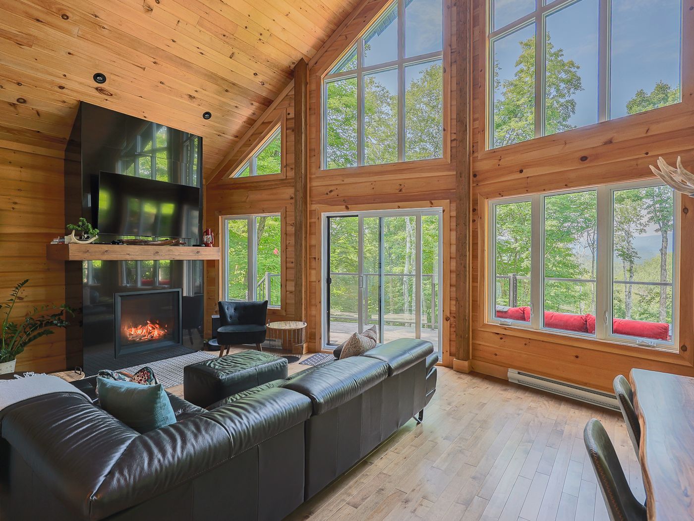 A spacious living room with a fireplace, leather sofa, and large windows offering a view of the outdoors.