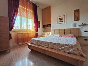 Ein Schlafzimmer mit Bett, Nachttisch, Kleiderschrank und einem Fenster mit Vorhängen.
