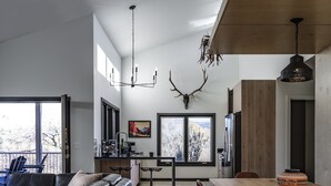 A modern kitchen with a wooden dining table, a black leather sofa, and a large window with a view of trees.