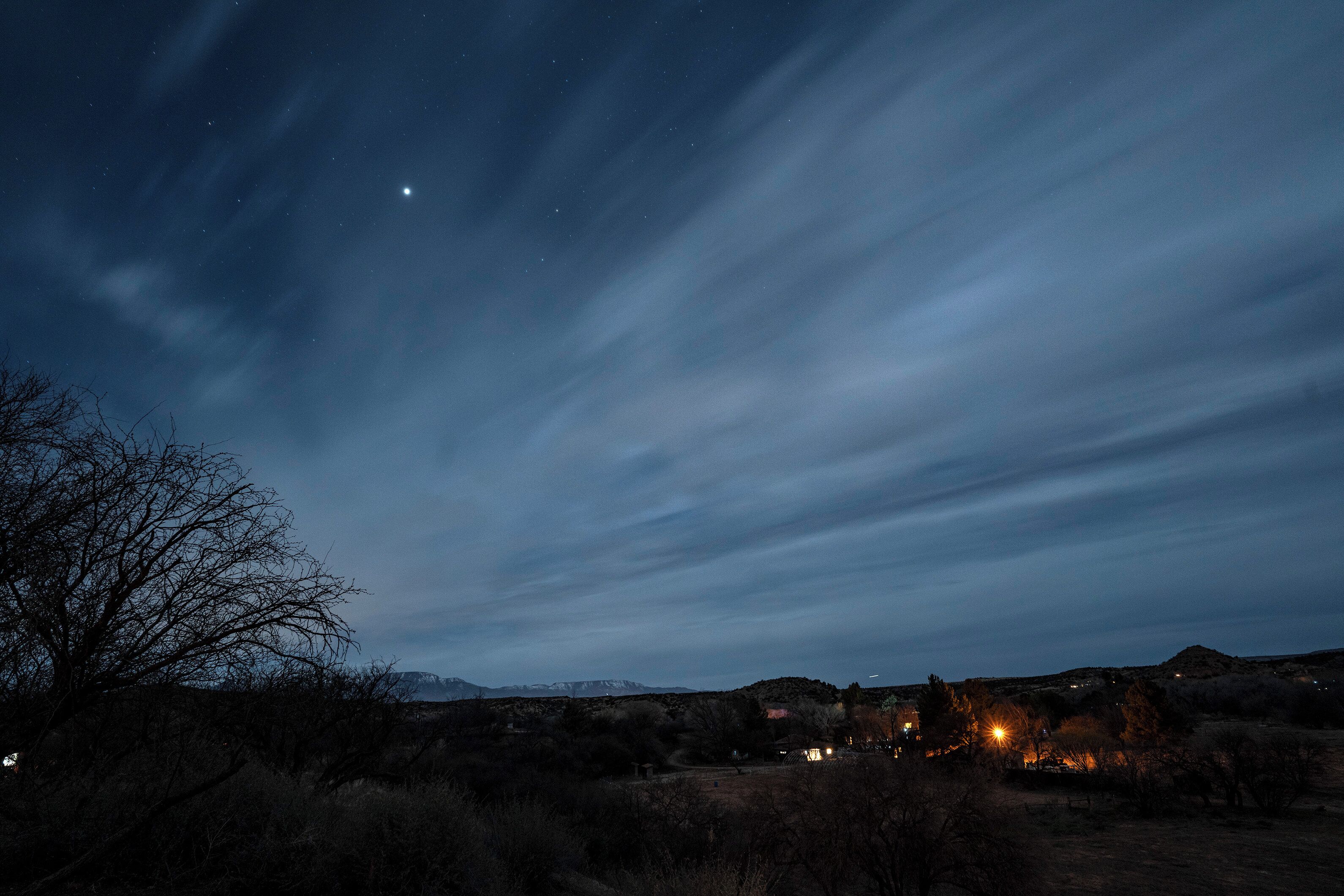 Un paysage nocturne avec un ciel dégagé, des étoiles et une chaîne de montagnes lointaine.