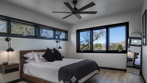 A modern bedroom with a large bed, wooden headboard, and a ceiling fan.