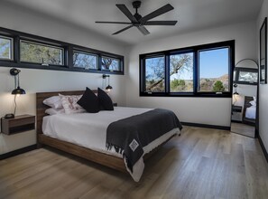 Relax in this serene bedroom with a large bed, ceiling fan, and a window offering a view of the surrounding landscape.