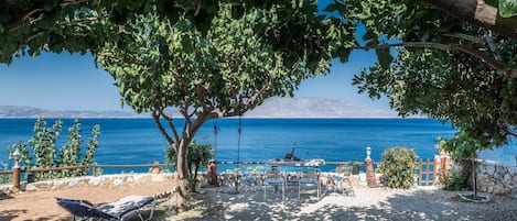 Un espace aménagé près de la plage, avec vue sur la mer, un arbre qui offre de l’ombre et un mur en pierre.