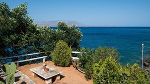 Eine Terrasse mit Tisch und Stühlen mit Blick auf das klare, blaue Meer, umgeben von Grünpflanzen.