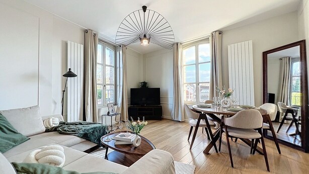 A modern living room with a sofa, coffee table, dining table, and chairs. There is a television and a plant in the room.