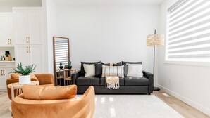 Ein modernes Wohnzimmer mit einer schwarzen Couch, einem braunen Sessel und einer Stehlampe.