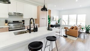 Une cuisine moderne avec des armoires blanches, des appareils en acier inoxydable, un robinet noir et un grand îlot central doté de tabourets.