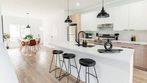 Une cuisine moderne avec des meubles blancs, un îlot central doté de tabourets et un éclairage suspendu.