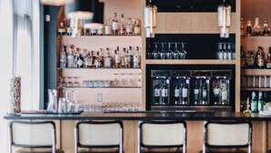 Un espace bar avec des étagères remplies de bouteilles d’alcool et de verres, un comptoir et des tabourets de bar.