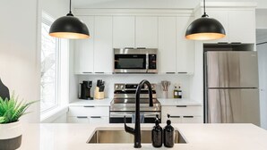 Een moderne keuken met witte kasten, roestvrijstalen apparatuur, een zwarte kraan en hanglampen.