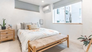 A bedroom with a bed, bedside table, bench, and potted plants.