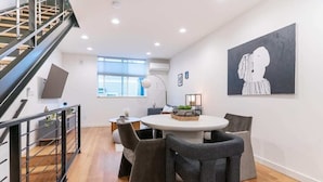 A modern dining area with a round table, grey chairs, and a staircase with metal railings.