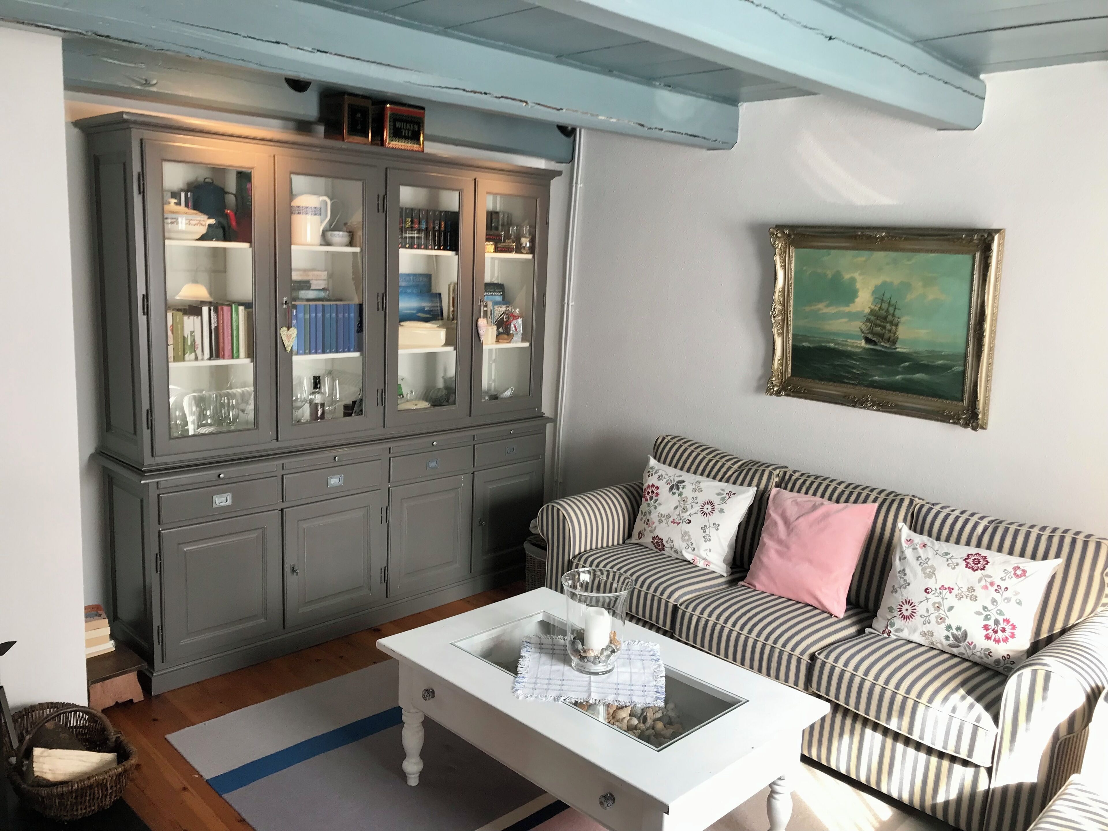 A living room with a striped sofa, a white coffee table, and a grey cabinet with glass doors.