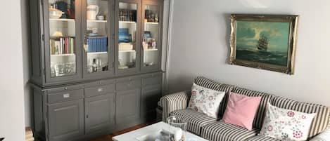 Un salon avec un canapé à rayures, une table basse blanche et un meuble gris aux portes en verre.