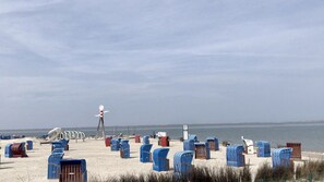 A beach with rows of numbered beach chairs and a windmill in the background. - Ruhe und Erholung pur um dem Alltagsstress zu Entfliehen, Friesenhaus mit Garten (Dornum)