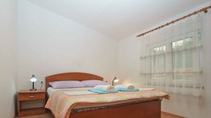 A bedroom with a wooden bed, two bedside tables, a night lamp, and a window with sheer curtains.
