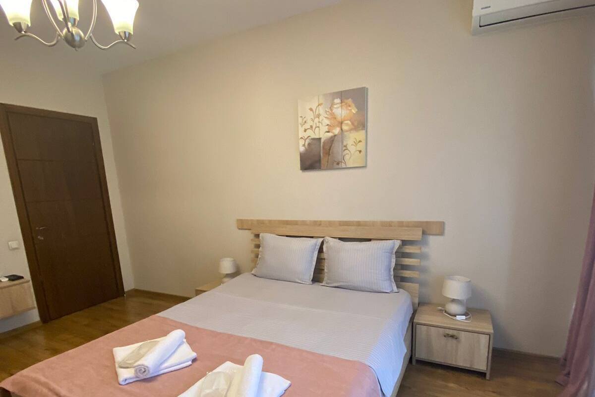 A hotel room with a bed, a nightstand, a wall-mounted air conditioner, and a ceiling light fixture.