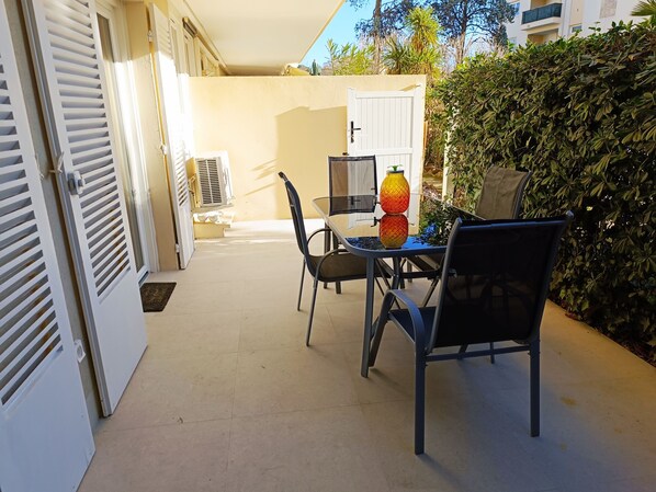 An outdoor patio with a table and chairs, a decorative vase, and a white door.