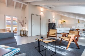 Ett modernt vardagsrum med en soffa, två trästolar, ett soffbord och ett kök i bakgrunden.