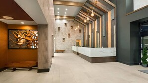 Un hall d’entrée spacieux avec un comptoir d’accueil, une grande œuvre d’art abstrait et un mur en briques.