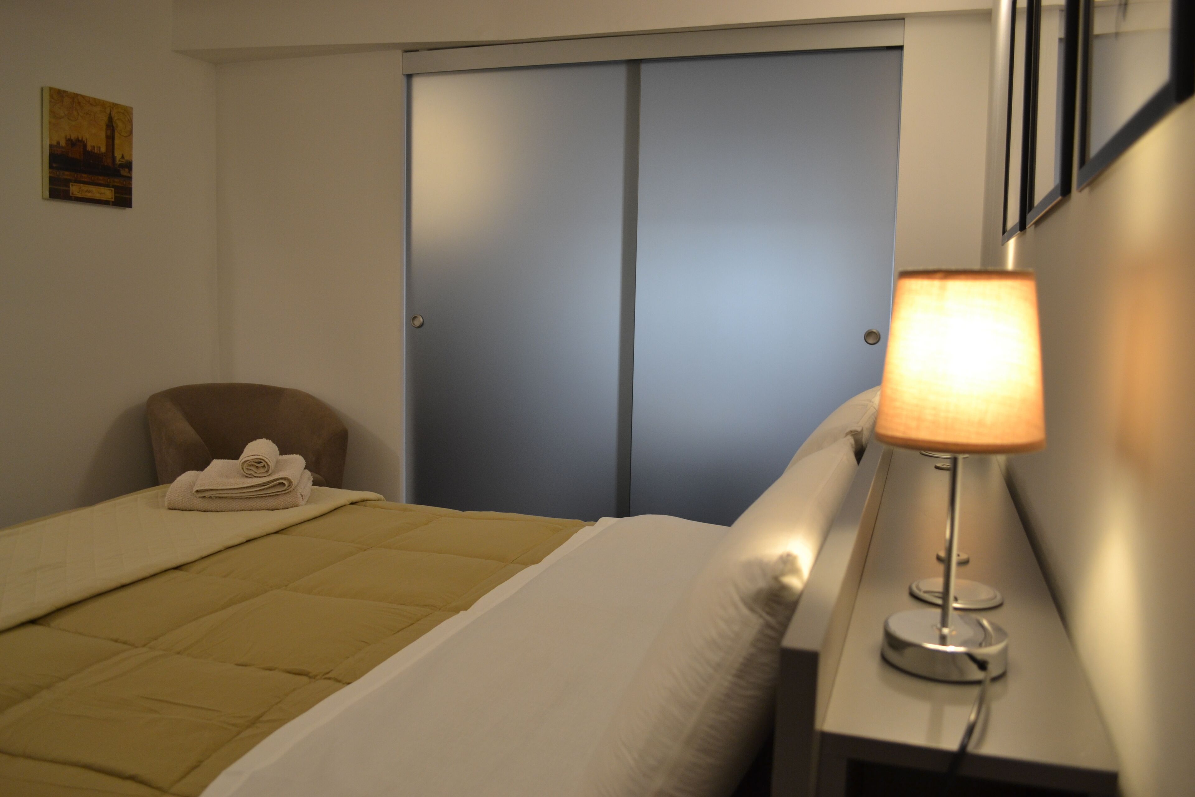 Une chambre d’hôtel avec un lit, une chaise, un bureau avec une lampe et une porte fermée.
