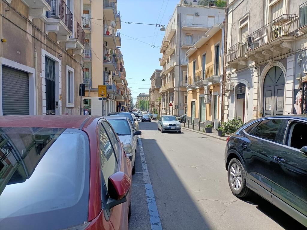 Eine Straße gesäumt von parkenden Autos und mehrstöckigen Gebäuden mit Balkonen.