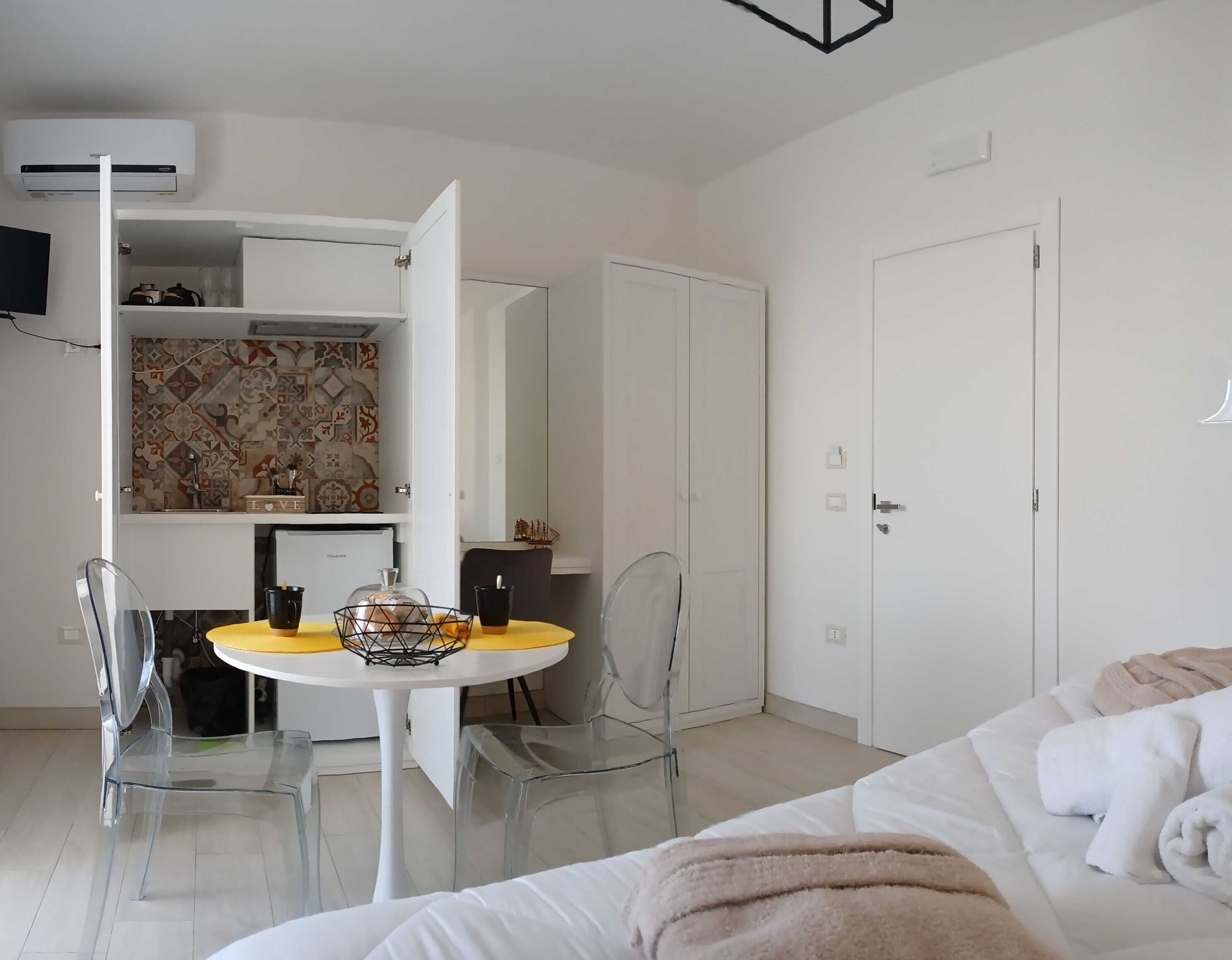 Een moderne hotelkamer met een bed, een eettafel met stoelen, een keukenhoek en een kledingkast.