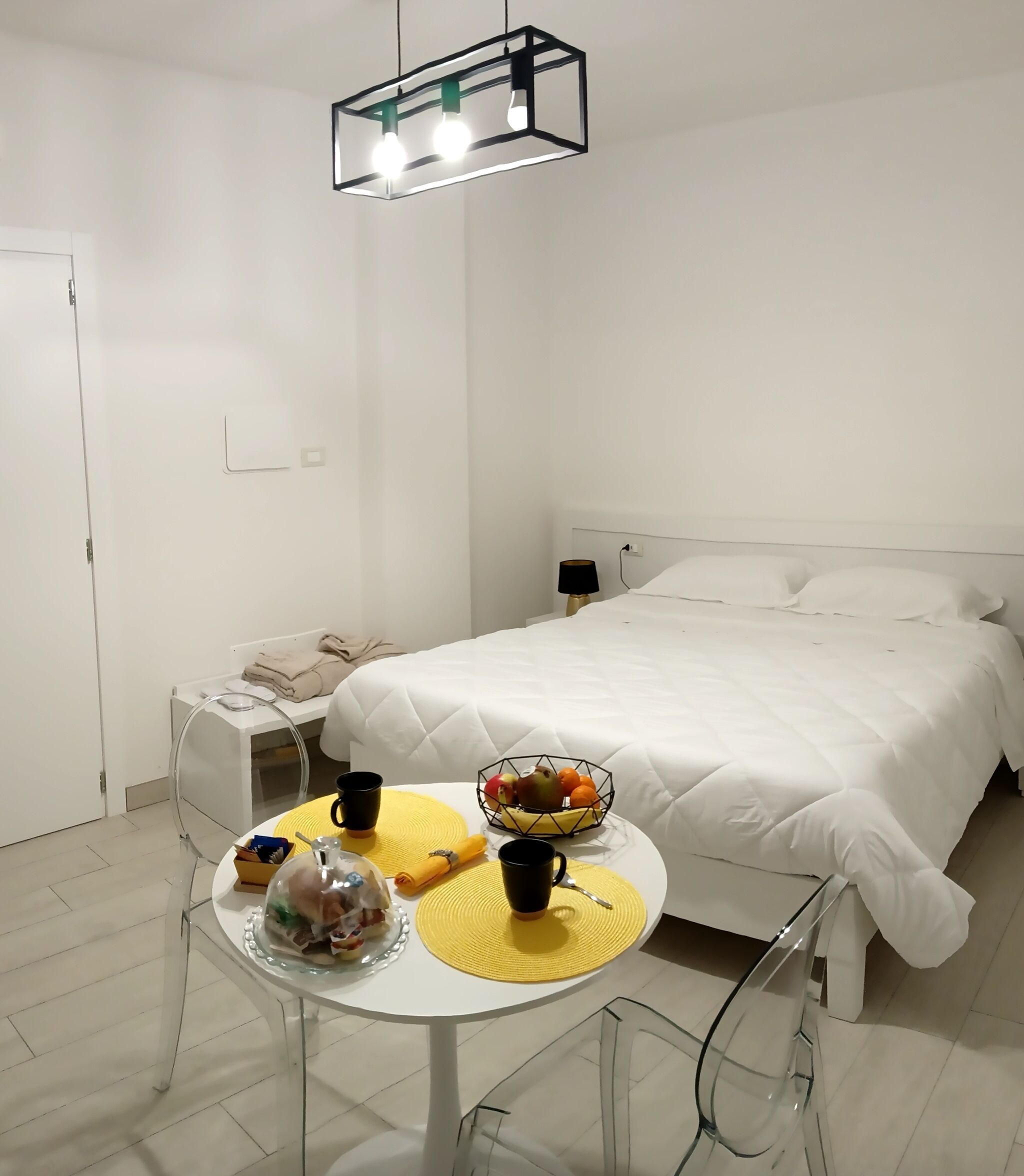 Habitación de hotel con cama, una mesa con alimentos para el desayuno y una lámpara colgante moderna.