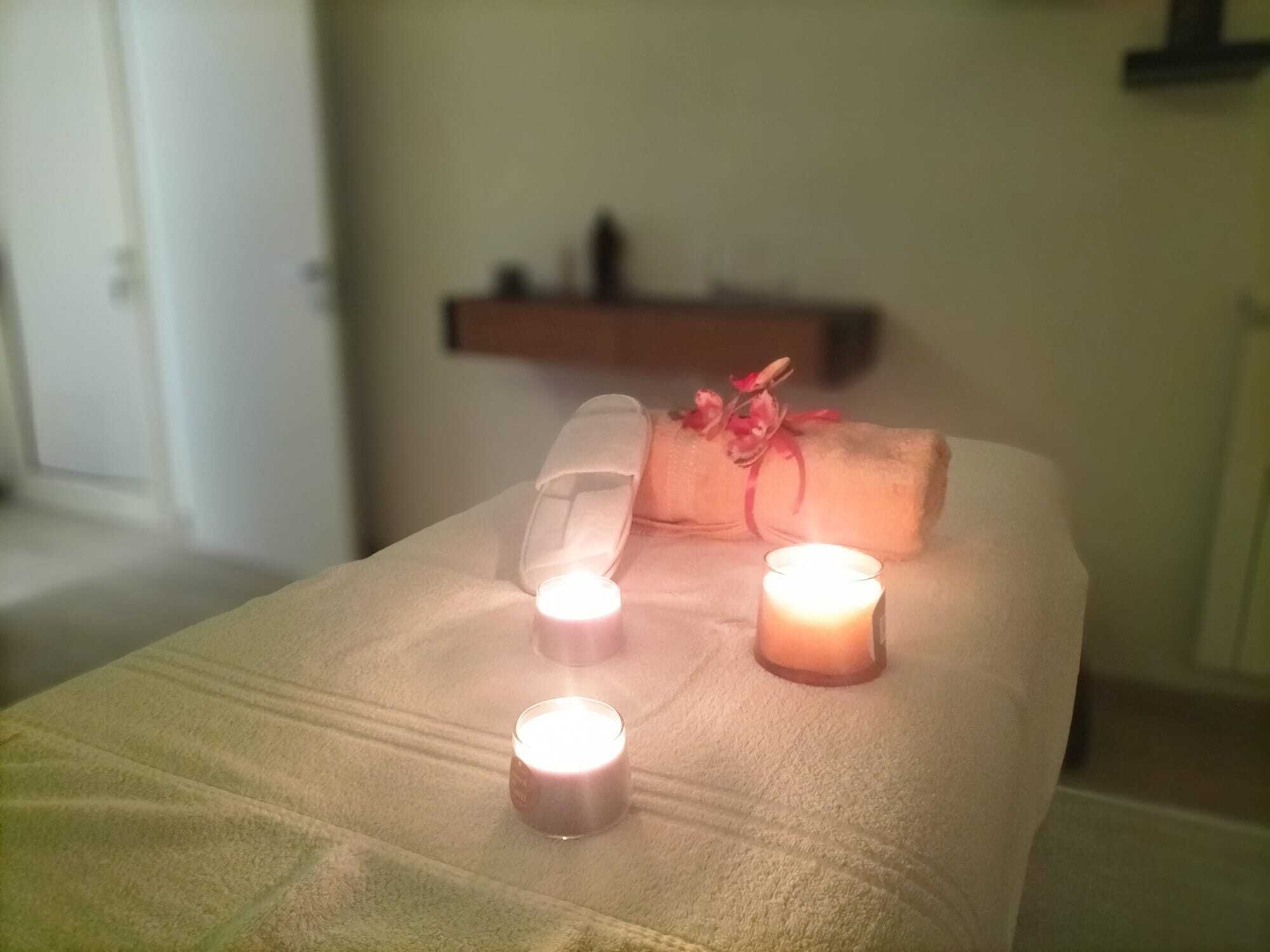 A neatly made bed with a rolled towel and two lit candles, suggesting a relaxing atmosphere.