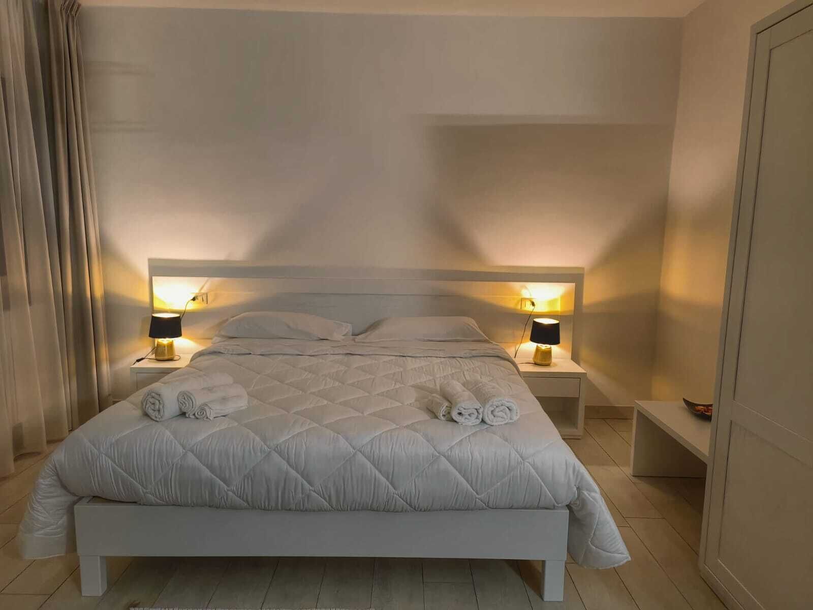 A neatly made bed with a quilted duvet, two bedside lamps, and a pair of towels on the bed.