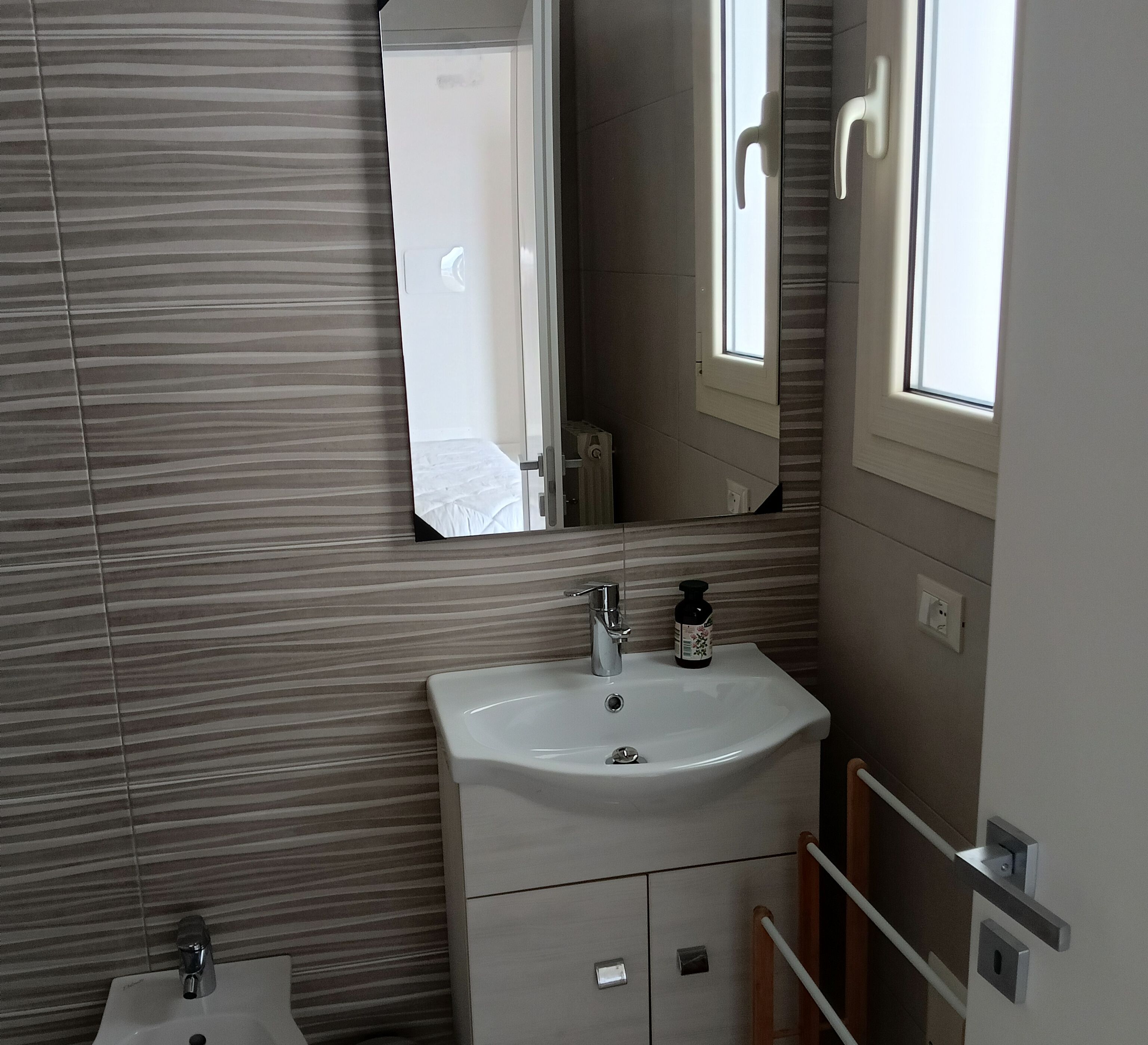 A bathroom with a white sink, a mirror above it, and a window with a view of a door.