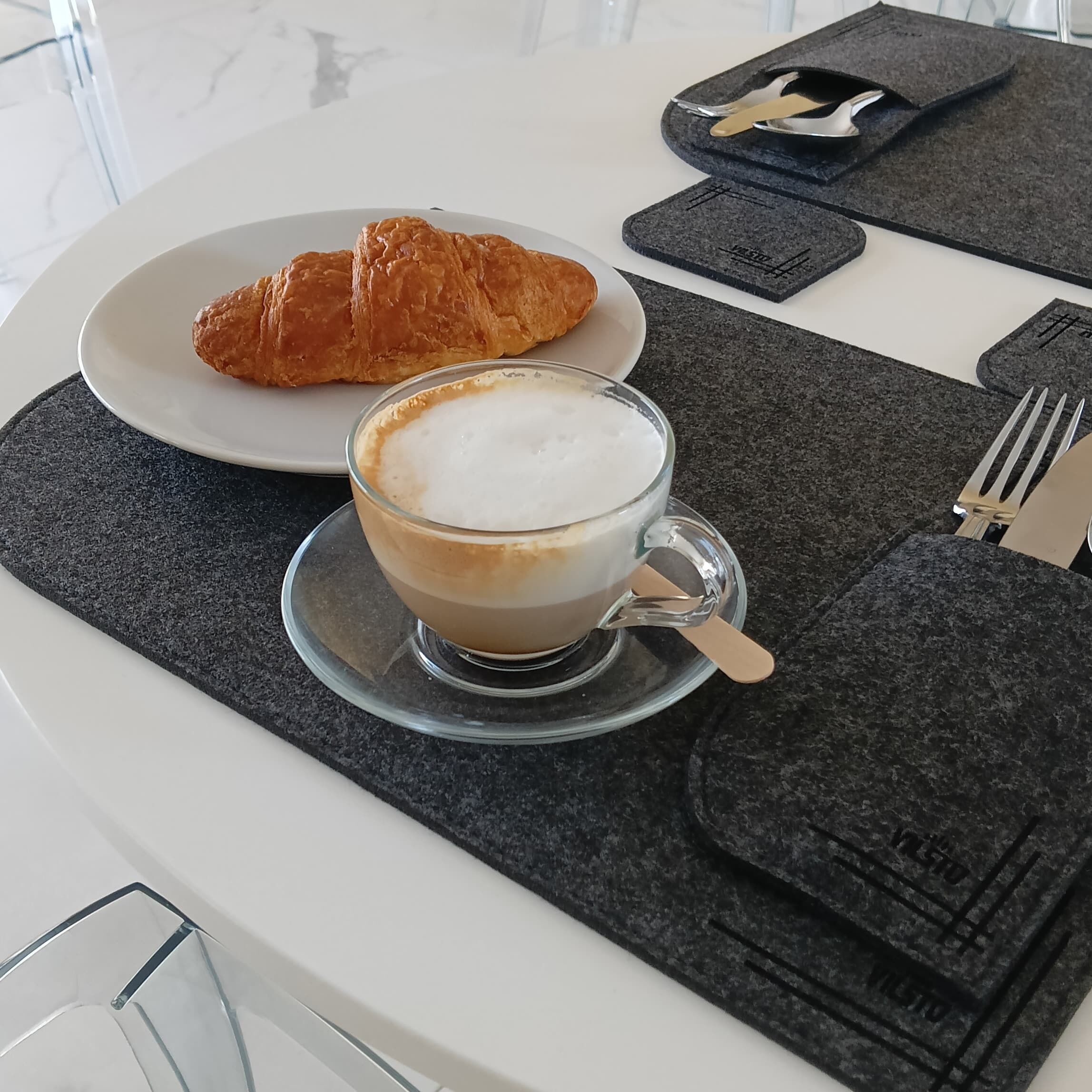 A breakfast setting with a croissant and a cup of coffee on a white table.