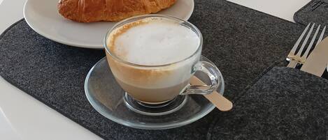 A breakfast setting with a croissant and a cup of coffee on a white table.